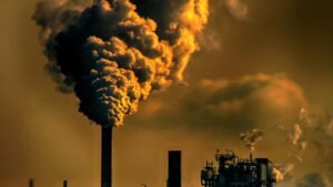 Industrial chimney emitting dark smoke against an orange sky