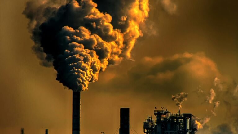 Industrial chimney emitting dark smoke against an orange sky